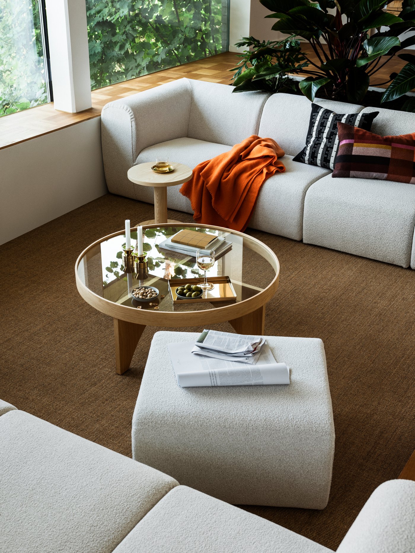 Ett mysigt, modernt vardagsrum med en vit sektionssoffa, ett runt soffbord i glas och en klarorange filt från kollektionen STOCKHOLM 2025.