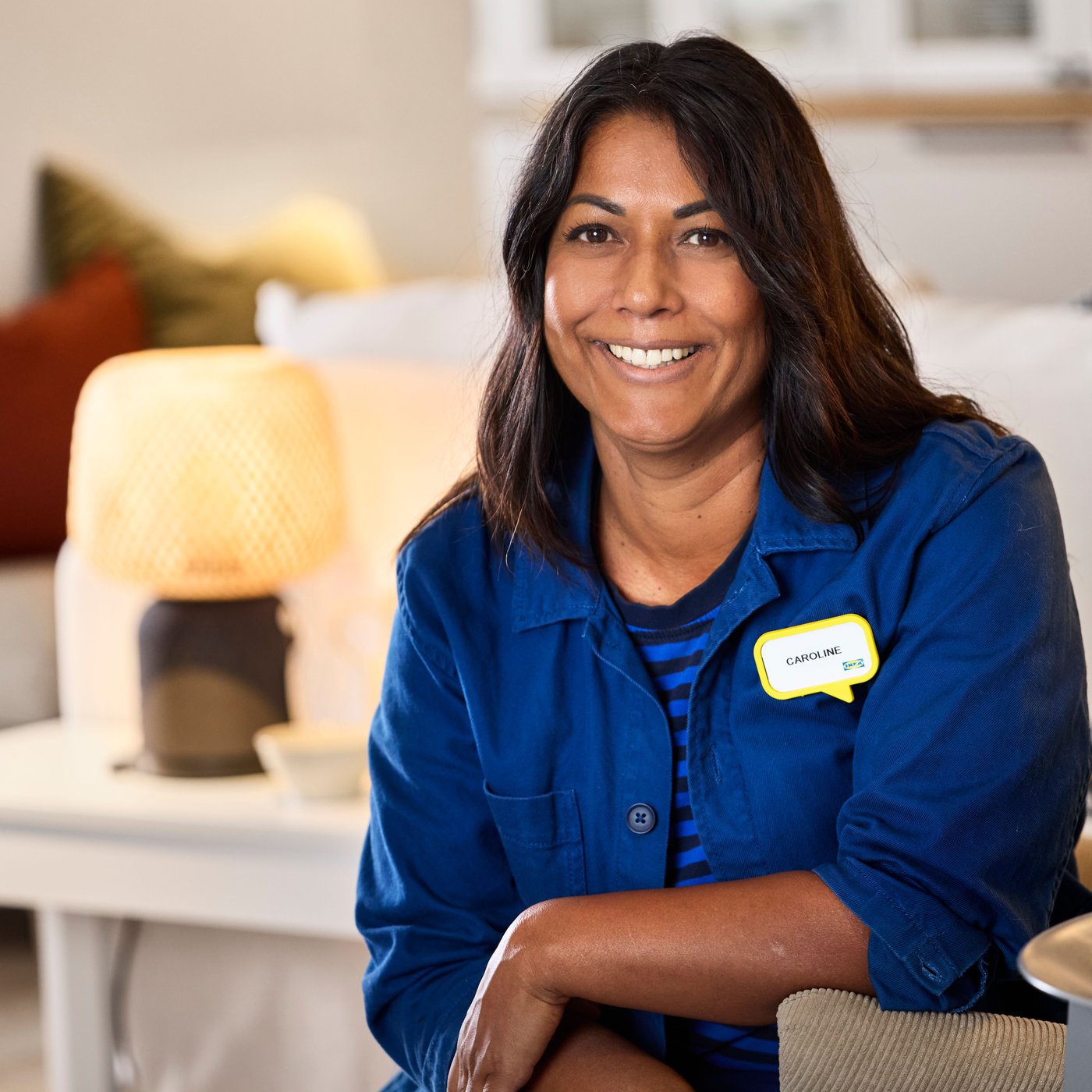 An IKEA interior designer wearing her blue work uniform sitting in a showroom smiling to the camera.