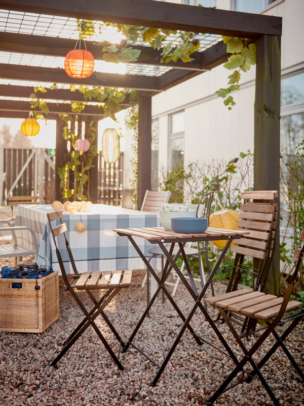 Een rij stoelen en kleine tafels die worden klaargezet voor een feest onder een versierde pergola op een binnenplaats.