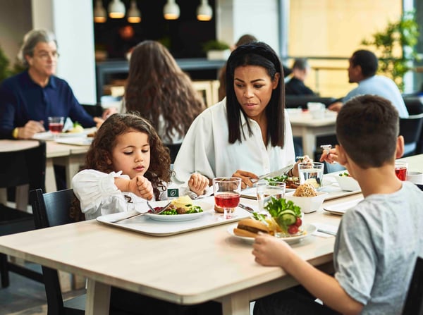 A family is enjoying a meal together in a restaurant. A woman and two children are sitting at a table with trays full of food. The atmosphere is relaxed and warm.