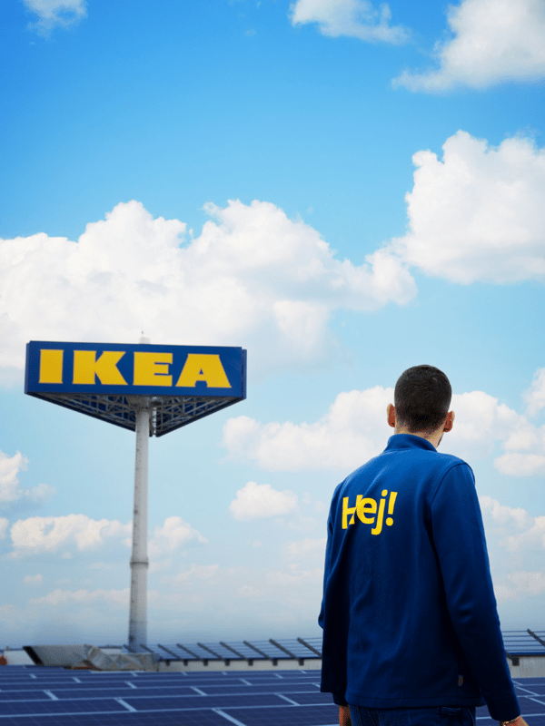 A co-worker stands in front of an IKEA sign, surrounded by solar panels under a clear sky.