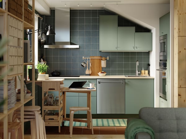A green L-shaped kitchen has grey green NICKEBO fronts and a RESARÖ mobile drop-leaf table with storage and some stools.