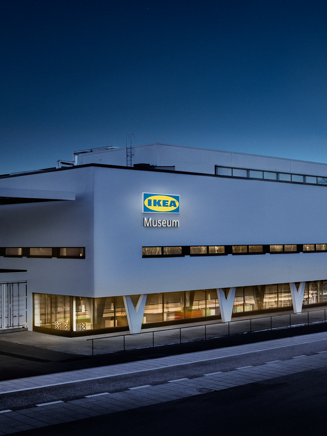 Bela zgrada IKEA muzeja obasjana plavom večernjom svetlošću.
