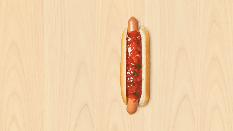 Ein Hotdog mit pikanter Soße liegt auf einem hellen Holzuntergrund.