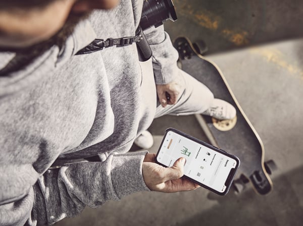 Muž stojí na skateboardu a v ruce drží mobilní telefon, na kterém je otevřená aplikace IKEA.