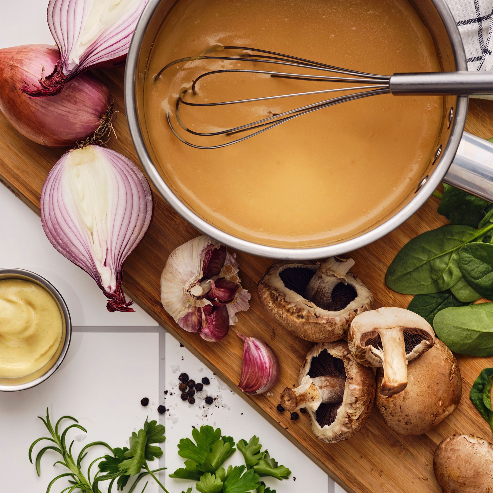 Na dasci za sečenje s belim lukom, pečurkama, začinskim biljem i ljutikom nalazi se žica za mućenje u šerpi s drškom u kojoj se nalazi ALLEMANSRÄTTEN mešavina za slani umak.