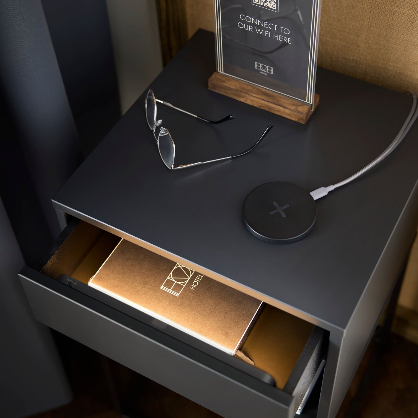 Un cassetto leggermente aperto del comodino dell'hotel è illuminato dolcemente da un'illuminazione a LED KÖLVATTEN super sottile, alimentata a batteria e dotata di sensore.