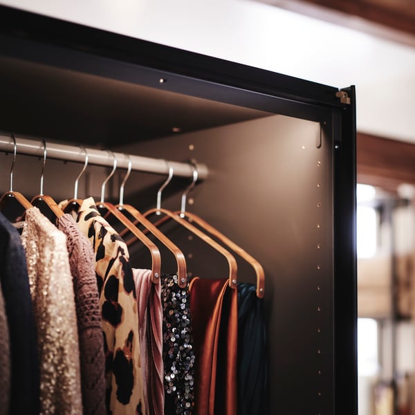 Close-up of PAX MEHAMN wardrobe with one of the sliding doors opened to show integrated lighting and clothes hanging inside.
