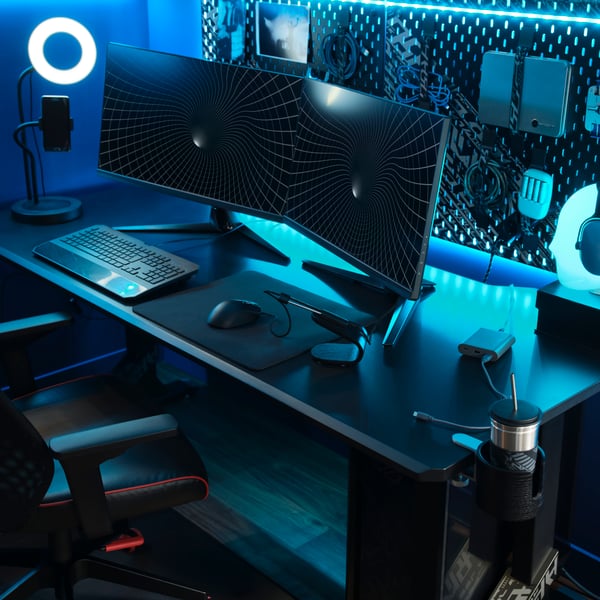 Osvetljen kotiček za gaming z zasloni, UPPSPEL gaming mizo ter kabli in pripomočki na UPPSPEL perforirani plošči.