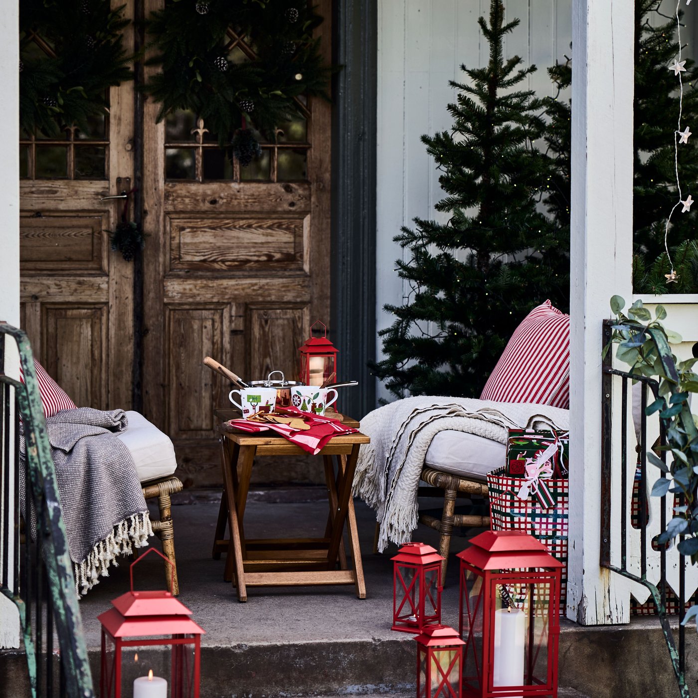 Christmas porch decor with striped red/white VINTERFINT cushion covers, red lanterns, a decorated Christmas tree, cozy chairs and festive accents.