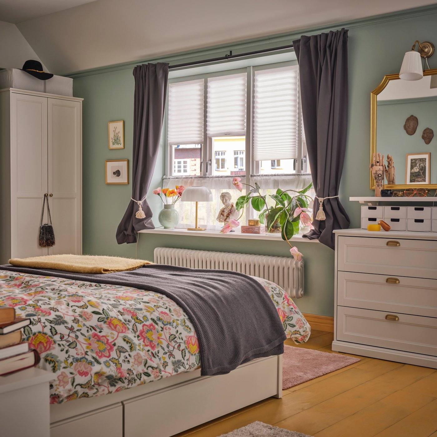 A bedroom with a bed with floral bed linen and a BEKVÄM stool near a window. KORGMOTT blackout curtains frame the window.