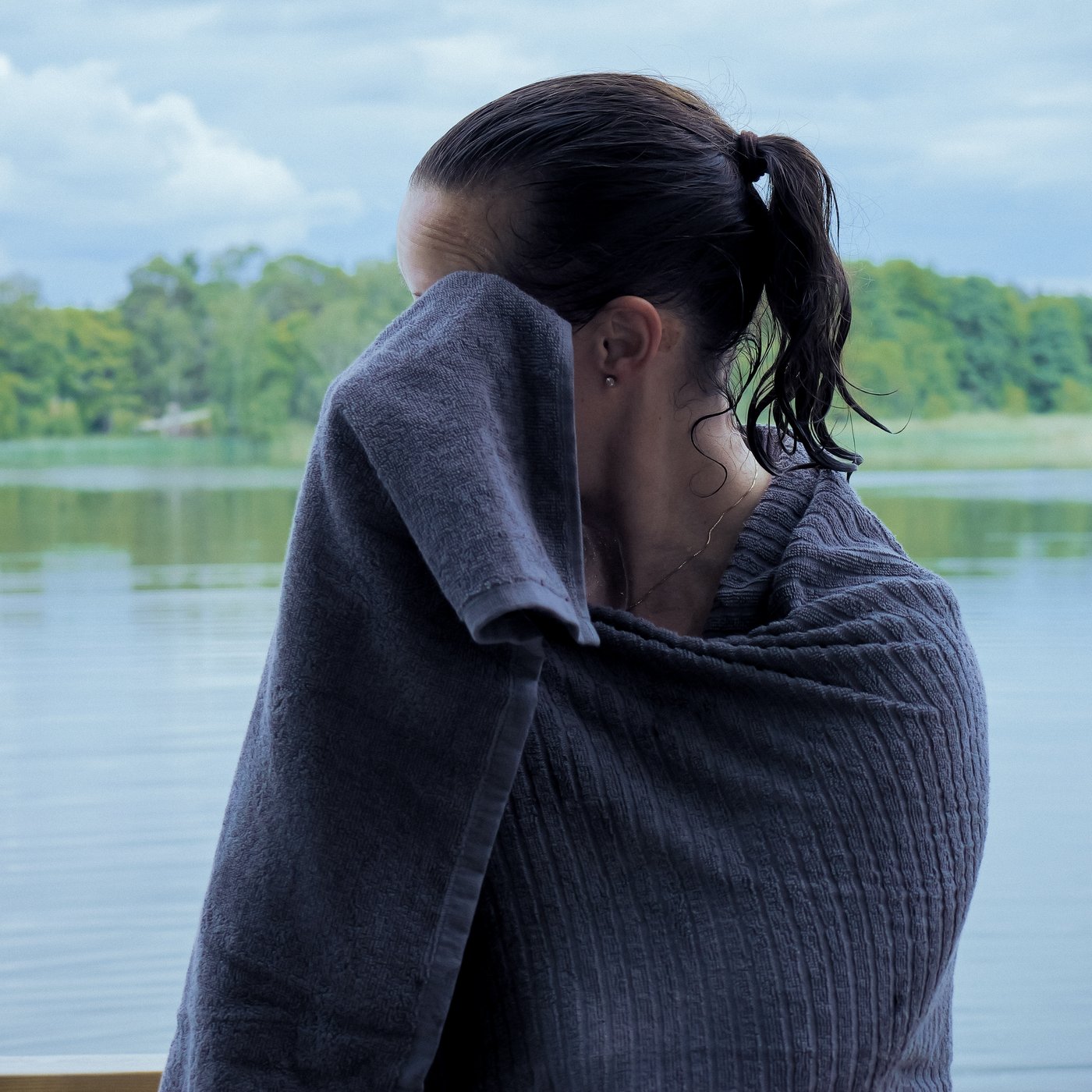 Una donna si asciuga il volto con un morbido asciugamano VÅGSJÖN dopo aver nuotato.