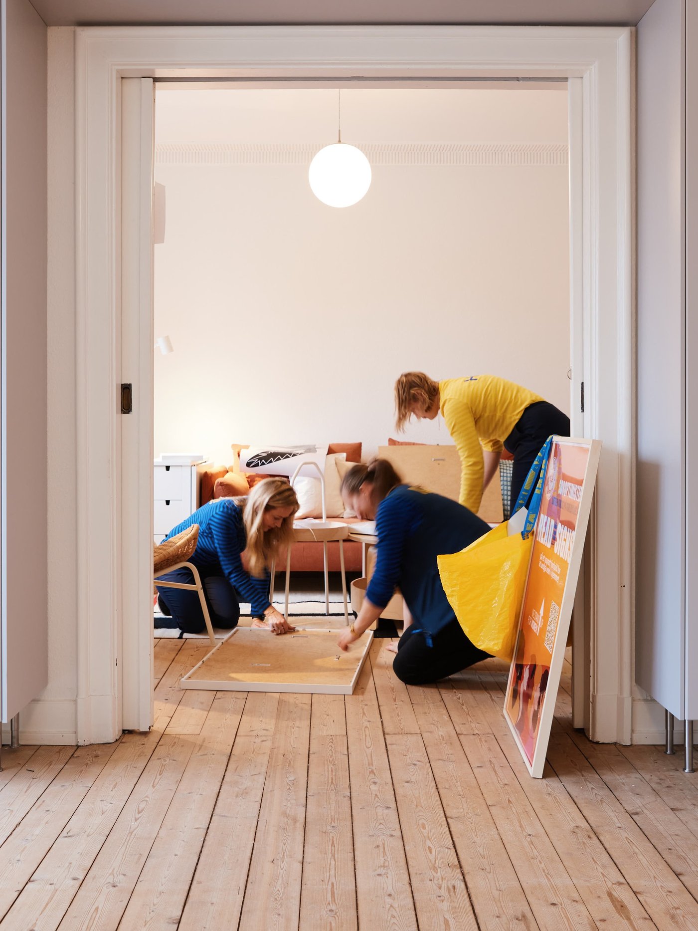 Flere mennesker fra IKEA Naboskab i gule og blå IKEA trøjer bygger møbler i en tom lejlighed