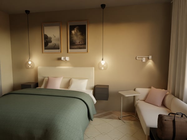 Teil eines Hotelzimmers. Ein Doppelbett mit Nachttischen. Über dem Bett zwei Bilder. Rechts neben dem Bett ein Sofa und ein Tisch.