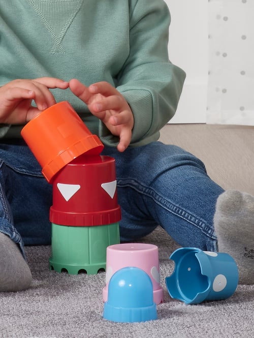 Multiple, multicoloured building breakers on a floor. A child is holding an orange building breaker above a stack.