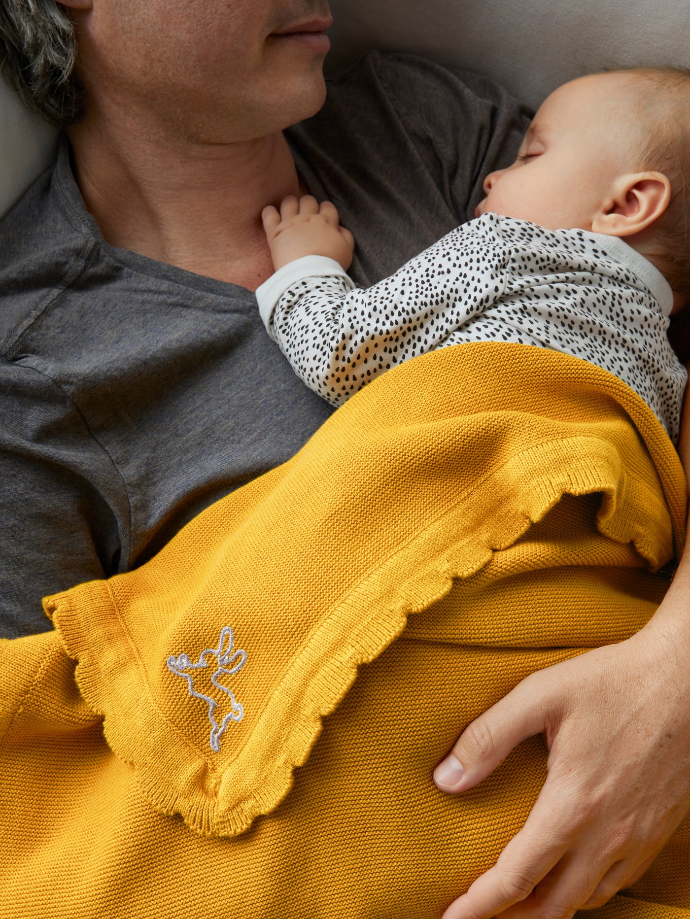 Part of the head and chest of a man who is holding a baby. The baby is wrapped in a dark yellow SOLGUL blanket.