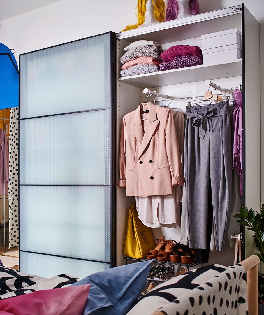 Ein Kleiderschrank mit Schiebetüren, u. a. mit einem PAX Rahmen für ein Schiebetürpaar und einem PAX Korpus für einen Kleiderschrank. Hinter der Tür ist förmliche Kleidung zu sehen.