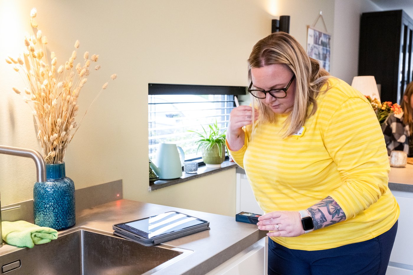 Osoba w odzieży służbowej IKEA wykonuje pomiar kuchni w domu u klienta.