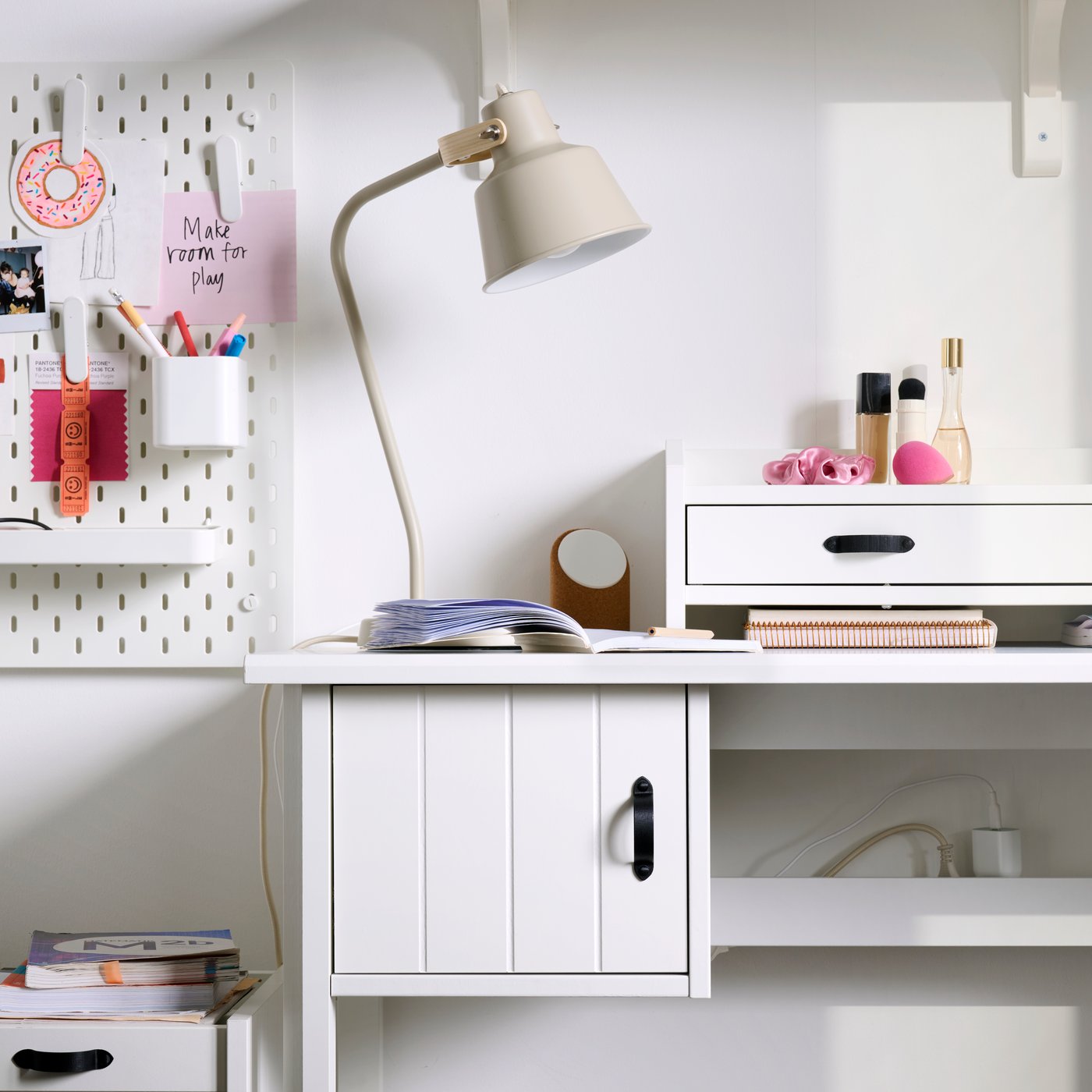 A workspace with a beige SJÖMAKT desk lamp made from ash illuminates a tidy desk with stationery and storage boxes.