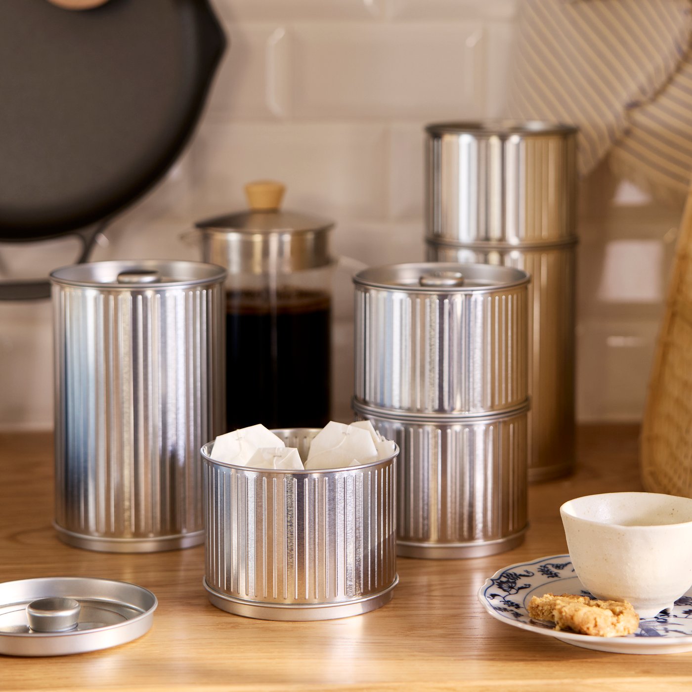 Silver-coloured tins with lids from the BETTHAJ series are placed on a worktop and some of them are stacked.
