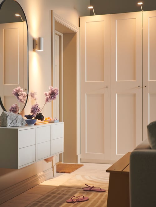Bedroom with a white up and down wired-in wall lighter made of steel placed next to a mirror, above a cabinet with 2 drawers.