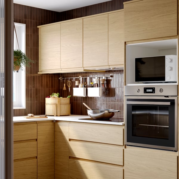 A kitchen with VOXTORP drawers fronts and doors in oak effect, ANRÄTTA forced air oven in stainless steel, baskets hanging.