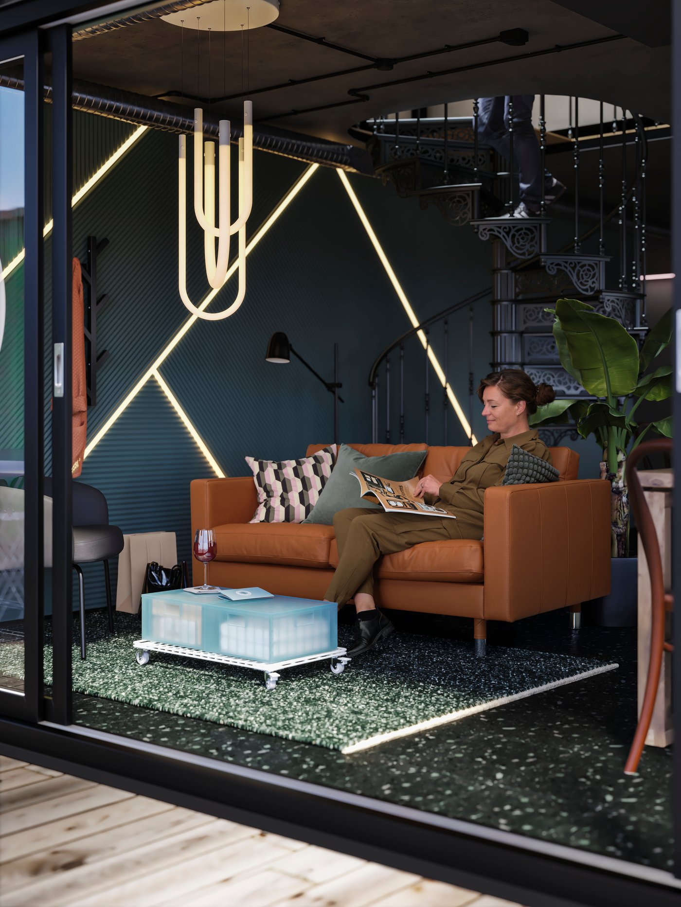 A person wearing a brown jumpsuit is sitting in a LANDKRONA sofa reading magazine in a space with dark grey walls.