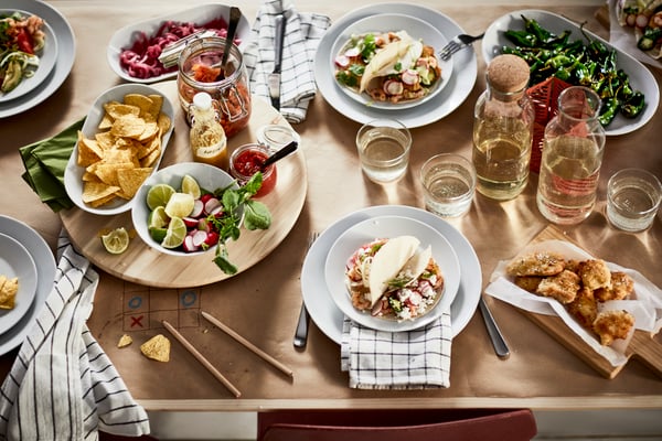 Una tavola preparata per accogliere gli ospiti con piatti bianchi IKEA 365+ di misure diverse e vassoi in legno con leccornie di ogni tipo