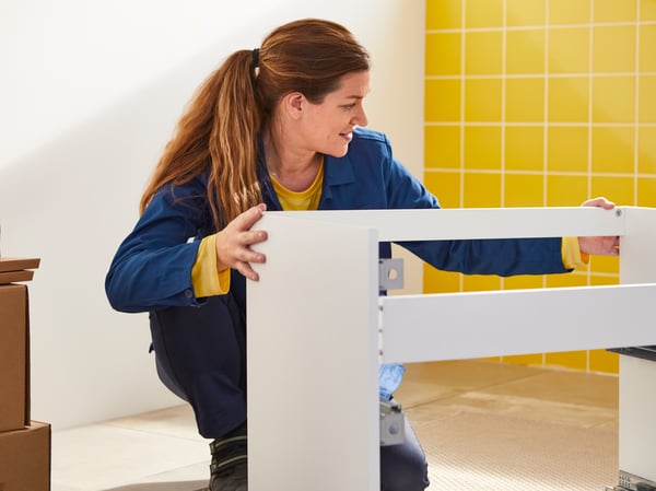 Un collègue d'IKEA est agenouillé sur le sol d'une salle de bain, tenant un pot de chambre blanc.