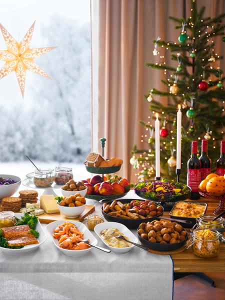 Ein weihnachtlich gedeckter Tisch mit vielen Speisen. Im Hintergrund ein geschmückter Weihnachtsbaum
