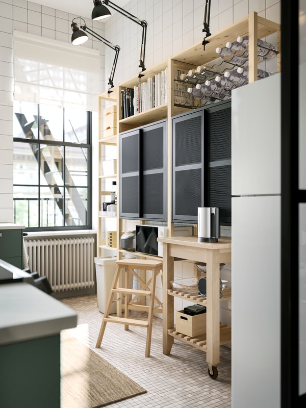 A pine IVAR shelving unit with two black mesh cabinets with doors and dark grey work lamps up top, plus a kitchen trolley.