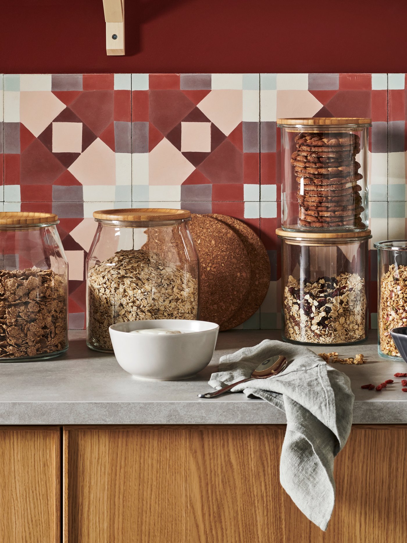 IKEA 365+ tarros de vidrio con tapas con cereales para el desayuno en la encimera de la cocina con azulejos geométricos y un estante en la pared.