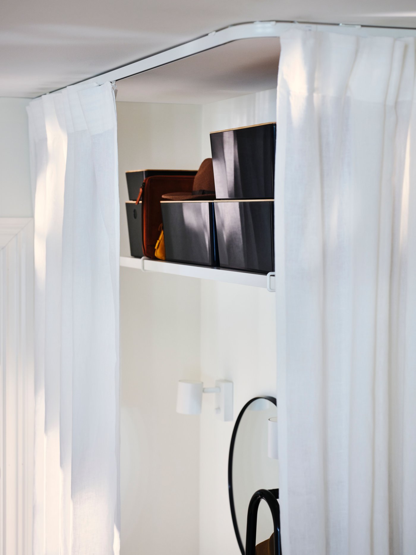 A white shelf holding five KUGGIS boxes with a mirror below it surrounded by a white DYTÅG curtain hanging from a VIDGA rail.