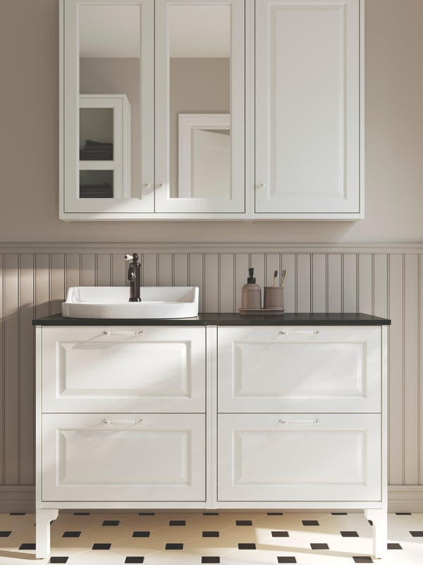Un baño gris claro con suelo a cuadros con dos muebles de lavabo TÄNNFORSEN blancos con una encimera con efecto mármol negro.