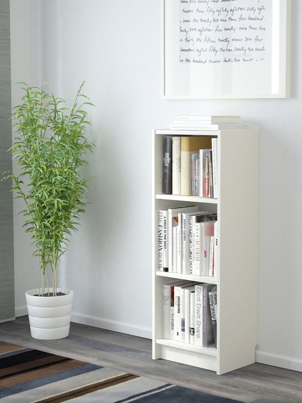Ein weißes BILLY Bücherregal  40 breit, 28 tief und 106 cm hoch, steht vor einer weißen Wand. Daneben steht eine Zimmerpflanze. 