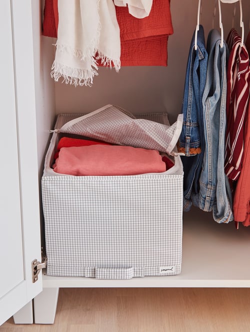 A bottom shelf in wardrobe has a white/grey STUK storage case that is slightly unzipped to show clothes inside.