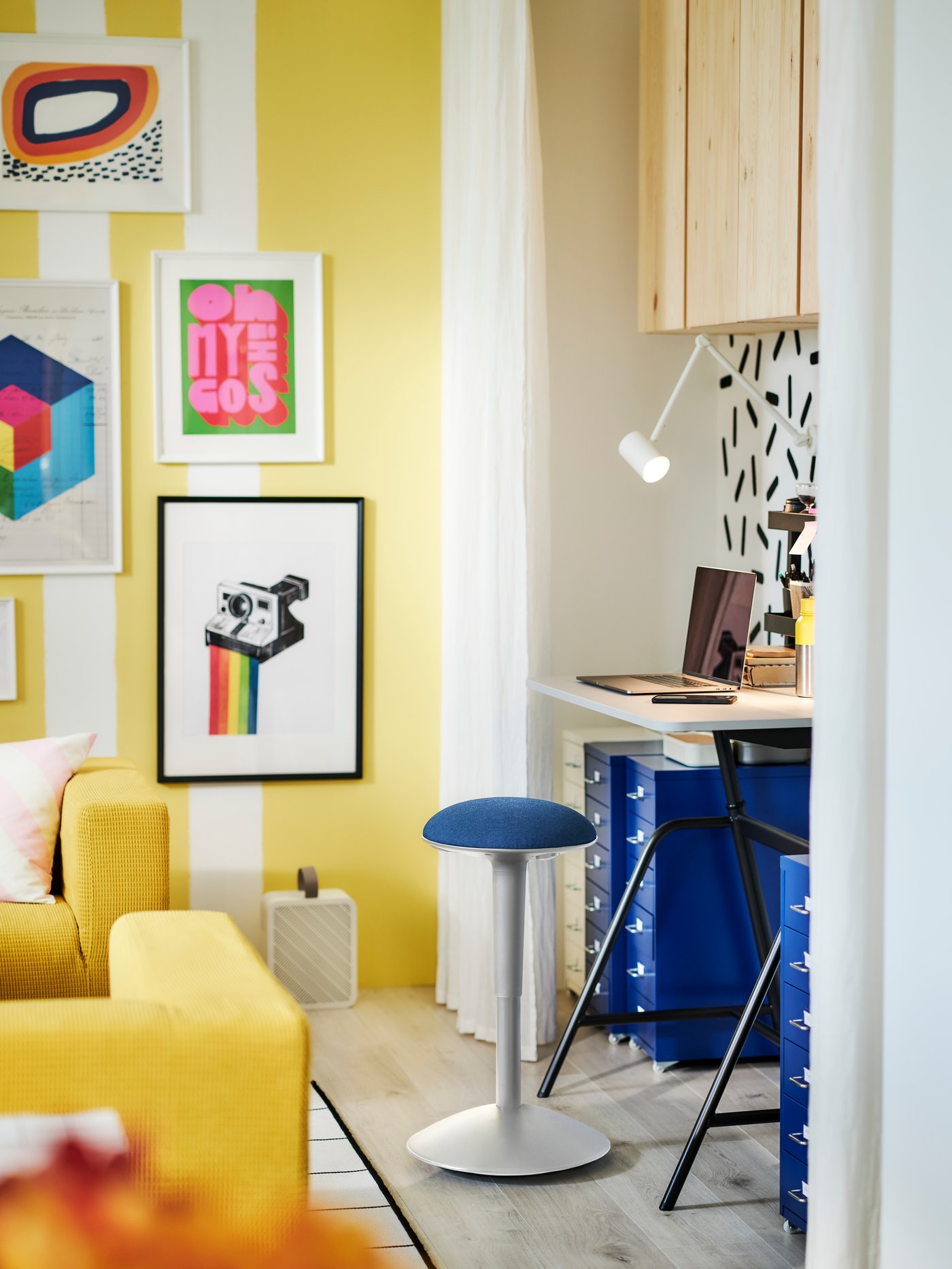 Una habitación colorida con un espacio de trabajo flanqueado por cajoneras con ruedas HELMER azules y un soporte de pie NILSERIK.
