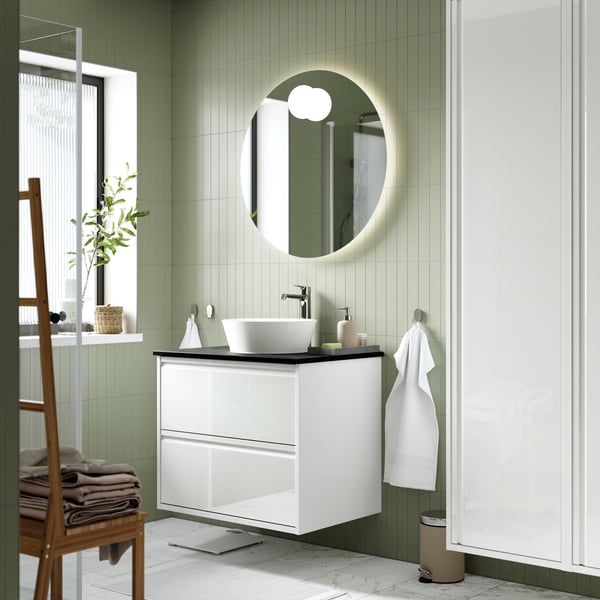 A bathroom with green walls has a white ÄNGSJÖN vanity with drawers and a double sink and two mirror cabinets.