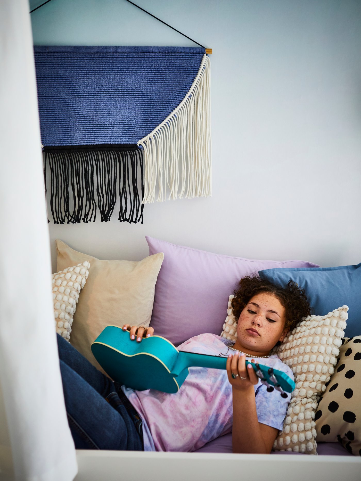 Habitación para bebés y niños con una persona tumbada sobre la funda de cojín cuadrada SVARTPOPPEL, rodeada de otras fundas de cojín.