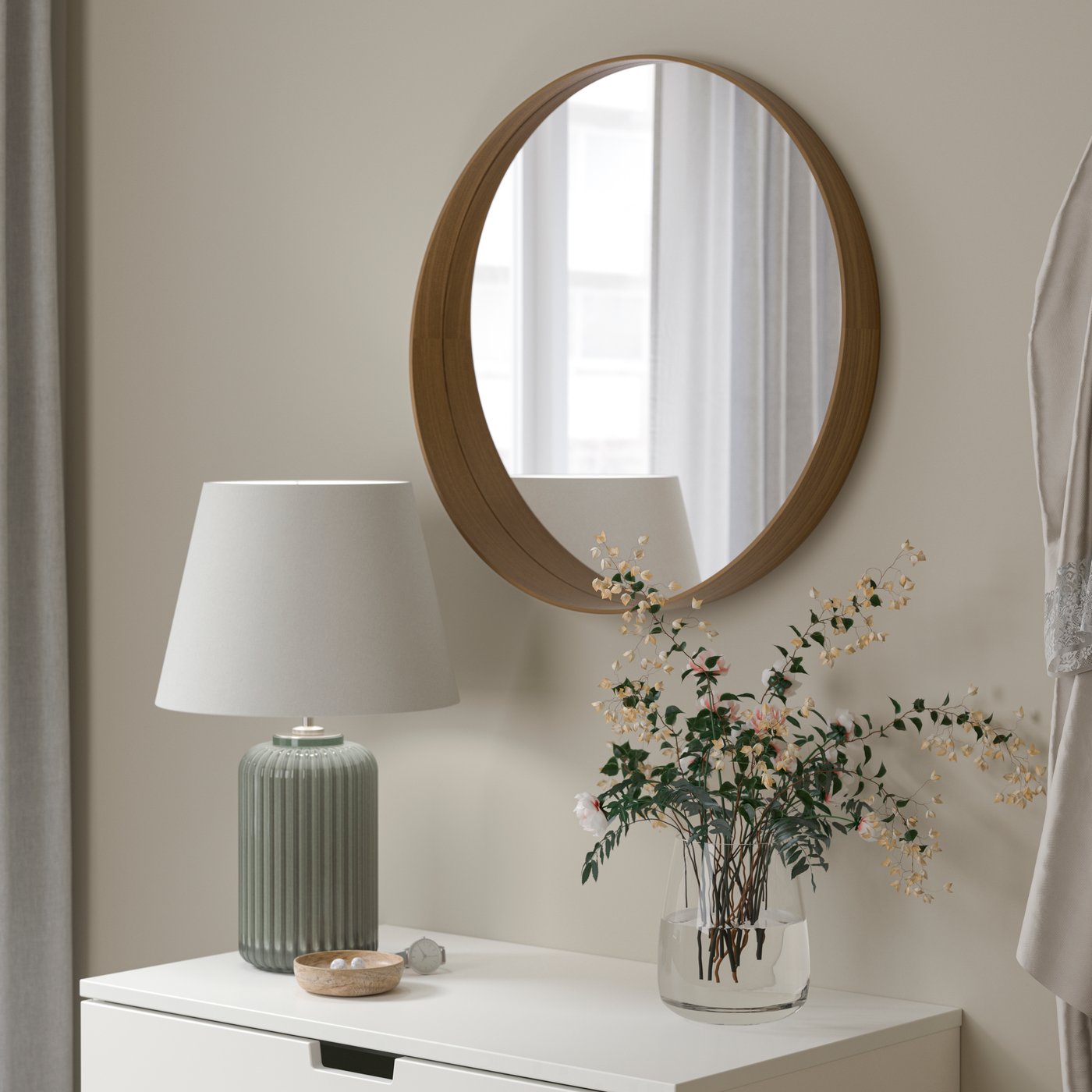 Een walnoothouten fineer STOCKHOLM ronde spiegel boven een dressoir met een tafellamp.