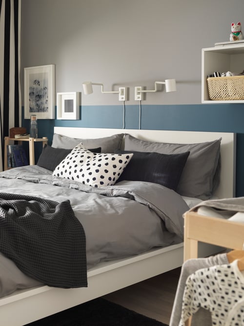 Bedroom with white bedframe, wall cabinet, shelving unit, quilt cover and pillowcases, bedspread, cushion cover, wall lamp.