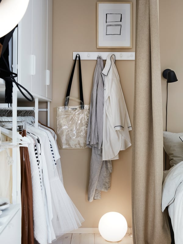 Clothes hang to get aired on a white LURT/GUBBARP rack with six knobs, mounted on the wall next to an open wardrobe.