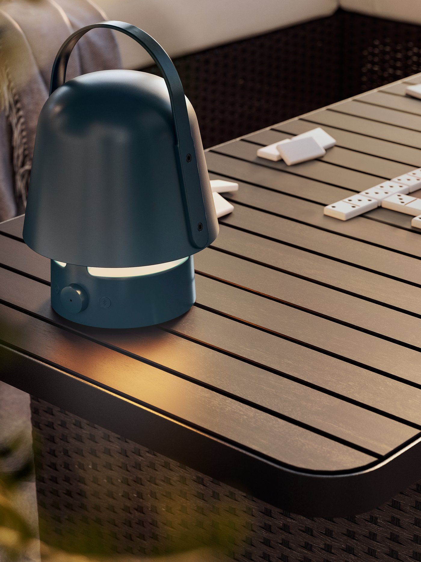 A dark blue VAPPEBY bluetooth speaker lamp for outdoor use on a dark grey VITTSKÄR coffee table. Afternoon light outdoors.