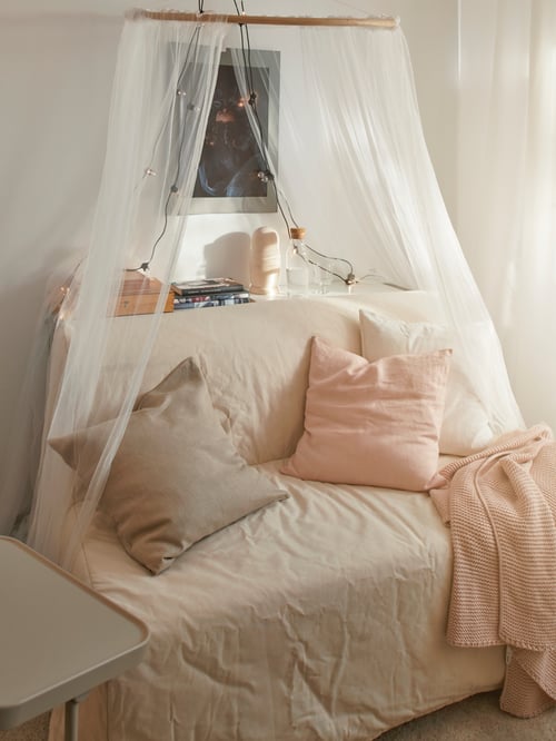 Living room with two seat sofa bed, laptop stand, cushion covers, cushions, throw, decorative objects, carafe, books, lamp.