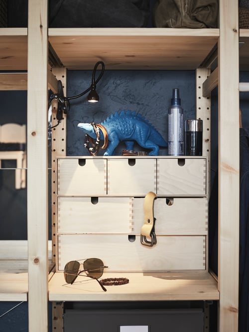 Bedroom area with a rectangular mini chest of drawers, a toy dinosaur, and a pair of sunglasses on a beige shelf.