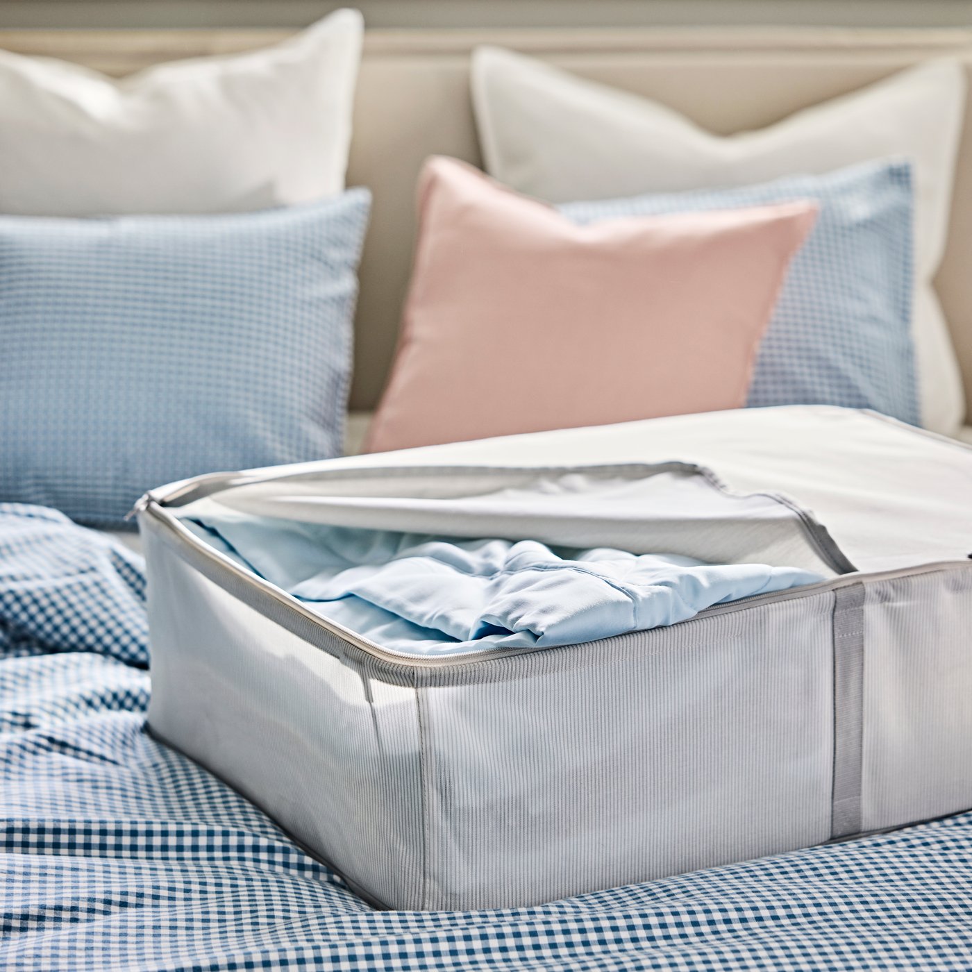 A HEMMAFIXARE storage base, containing bed textiles, is placed on a neatly made bed with a blue and while duvet cover.