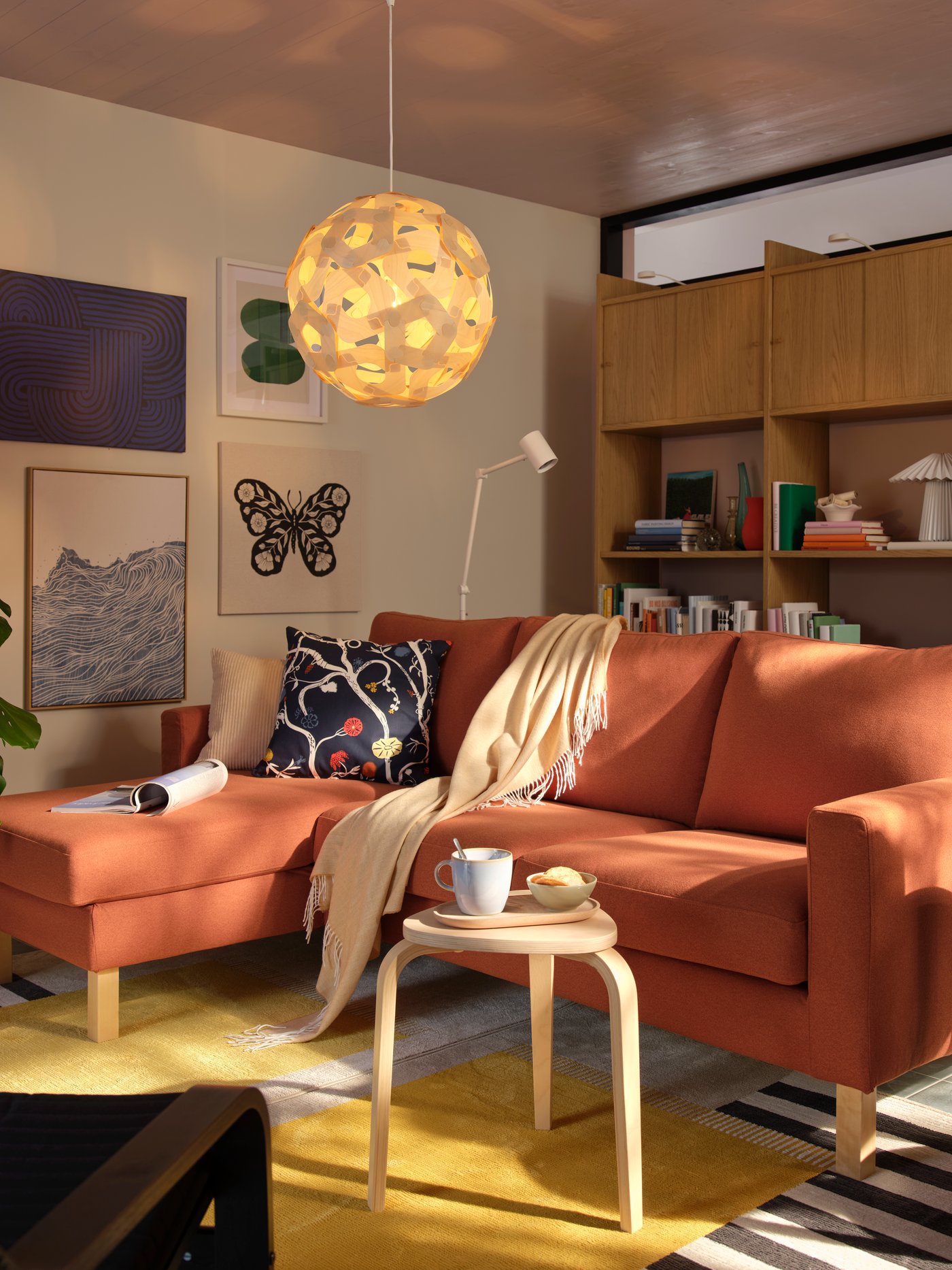 A living room with a red-brown SALTSJÖBADEN three-seat sofa with chaise longue, surrounded by modern decor and plants.