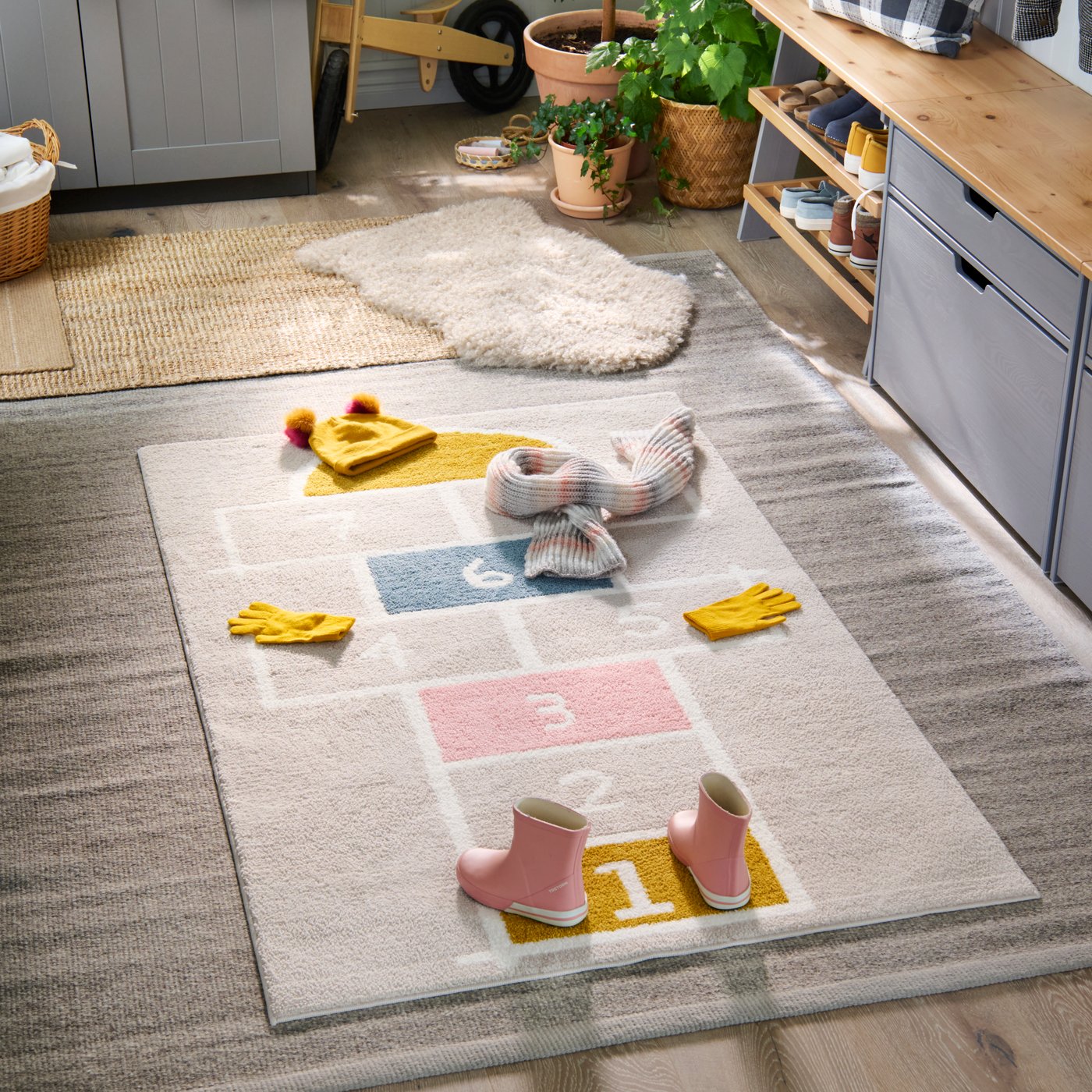 The floor of a hallway with STÄPPSPARV rug that has a hopscotch-pattern. Boots and stuff laid out on the different numbers.