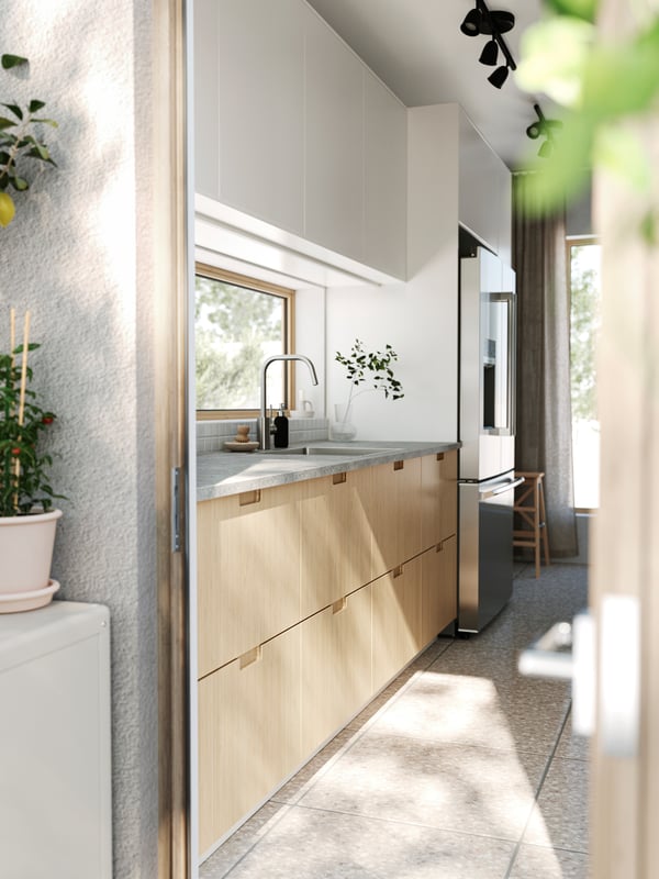 A patio door is open leading into a kitchen with stone floors, FÖRJERED fronts at the bottom and VEDDINGE fronts at the top.