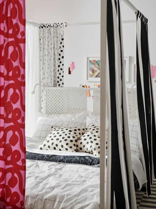 A white VITARNA four-poster bed with VARGTÖREL and FLUGBLOMSTER pre-cut fabric around it and VITKLÖVER bed linen on it.